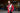 Person wearing a red jacket with championship belts in an indoor setting